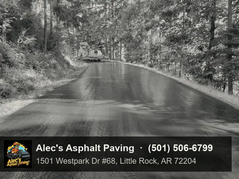 A freshly sealed, still-glossy road curving through the woods, with the road crew in the distance