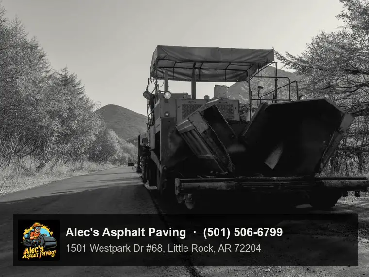 A hot-mix asphalt paver seen from the front with its hopper wings open, on a highway lined with autumn trees
