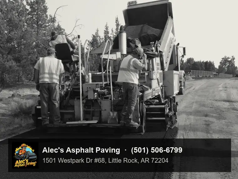 A hot-mix asphalt paver seen from behind, crew in hi-vis on the screed, laying fresh asphalt over a gravel base