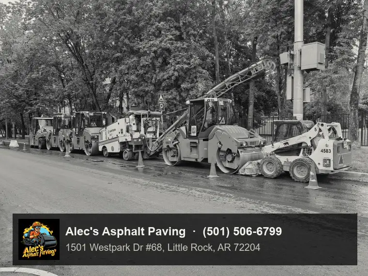 A row of rollers, a milling machine with its conveyor raised, and a skid steer parked along the curb of a wet, tree-lined street