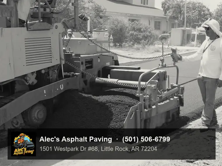 A screed operator standing beside a paver as hot mix spreads across the road