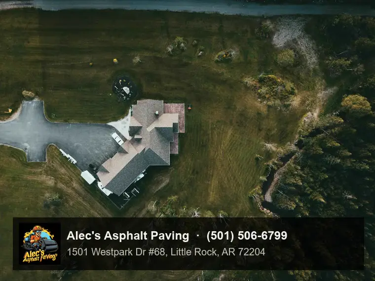 A drone view straight down on a rural house with a wide asphalt driveway and turnaround pad, set in mown fields beside woods and a creek