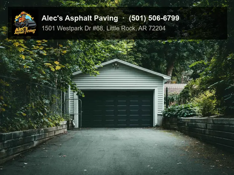 An asphalt driveway between timber retaining walls leading to a detached garage, under heavy trees