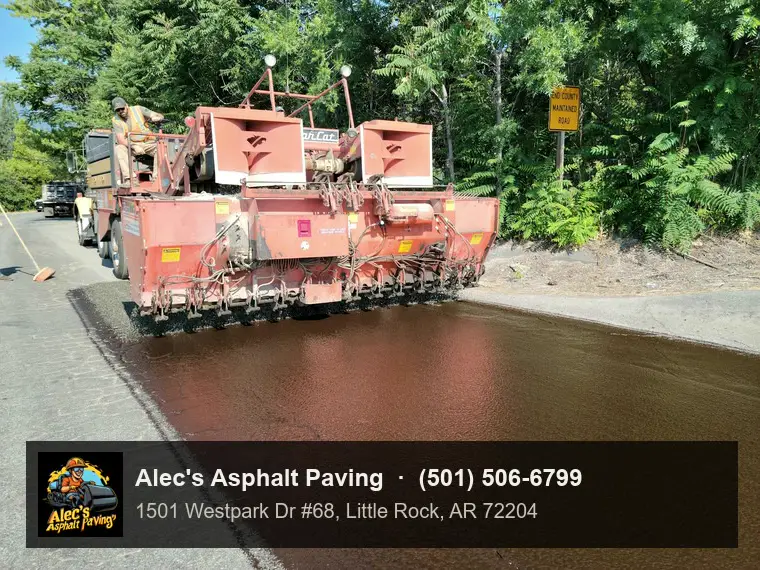 A chip spreader laying stone over fresh liquid asphalt on a country road