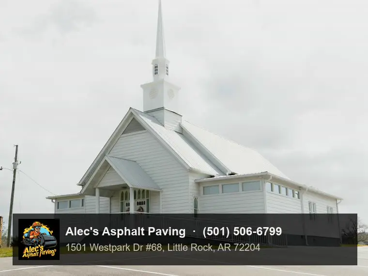 A small country church with a tall steeple and an accessible ramp, behind an asphalt parking lot with crisp stall lines