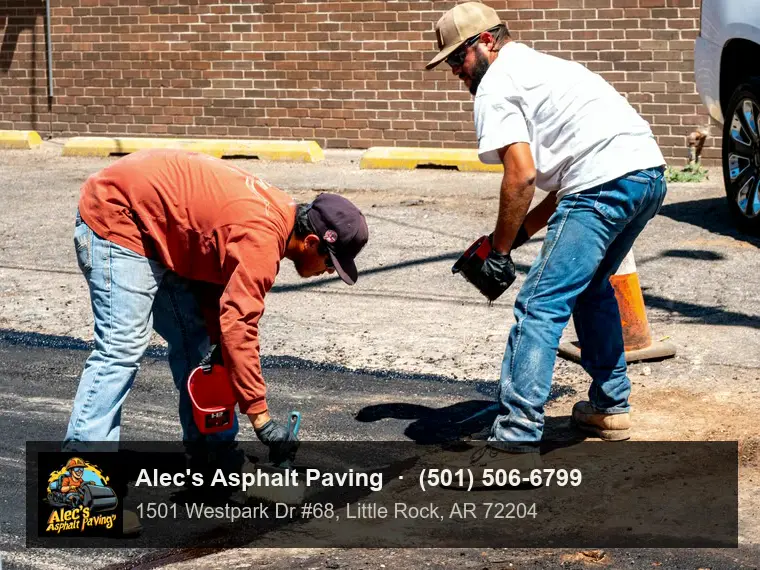 Two workers in a parking lot, one pouring sealant from a pour pot while the other brushes it into a seam in the asphalt