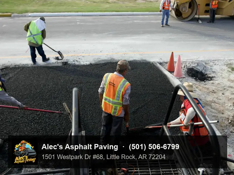A crew in hi-vis vests raking and shoveling hot mix along the edge of new asphalt