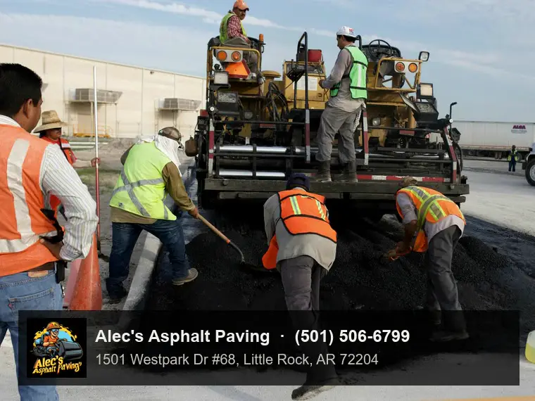 A crew in hi-vis vests raking and shoveling fresh hot mix behind a paver on a commercial lot