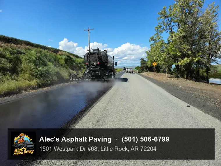 An asphalt distributor truck spraying a steaming lane of liquid asphalt on a rural road