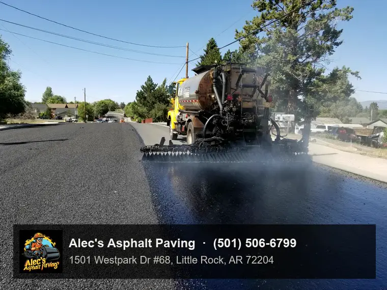 An asphalt distributor truck spraying a steaming coat of liquid asphalt across a residential street