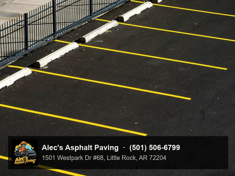 A jet-black parking lot with crisp yellow stall lines and concrete wheel stops along a black iron fence