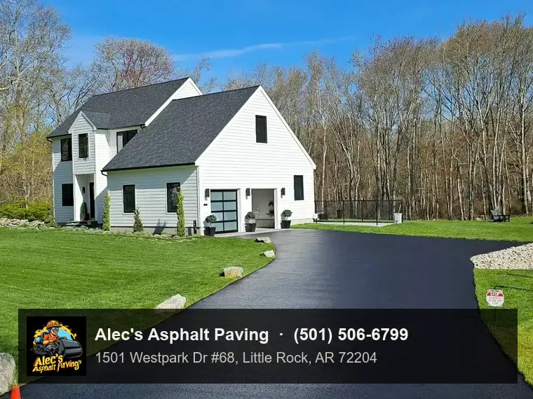 A freshly sealcoated black driveway curving up to a white two-story house, green lawn on both sides