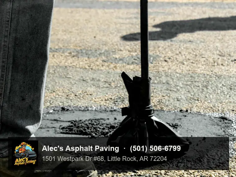 A worker beside a hand tamper, its head wrapped in black plastic, pressing down a fresh patch in a pothole on a stony road