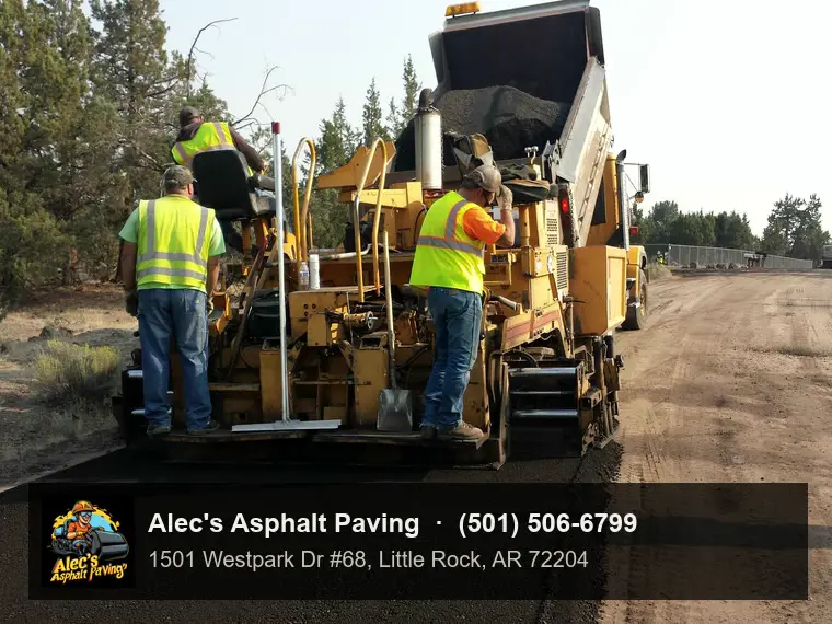 An asphalt paver seen from behind, crew in hi-vis on the screed, laying fresh asphalt over a gravel base