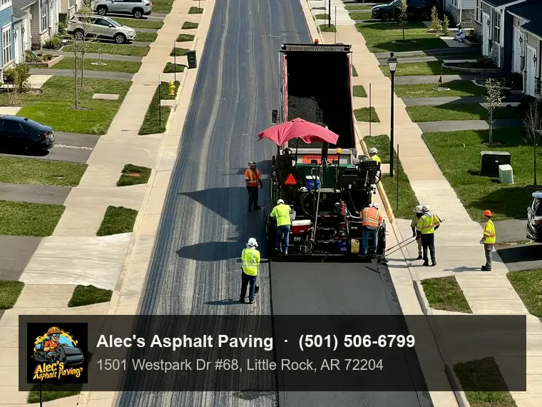 A paver laying a fresh black asphalt overlay down one half of a suburban street lined with townhouses, the old gray surface still on the other half