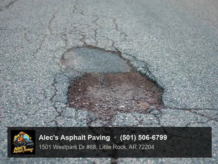 A pothole broken through an old asphalt road down to the stone base, with alligator and lengthwise cracks spreading from it