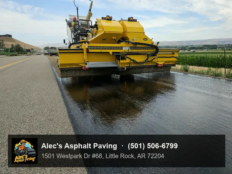 A chip spreader laying stone over freshly sprayed liquid asphalt on a two-lane rural highway